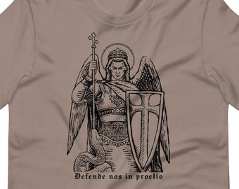 May include: A brown t-shirt with a black and white illustration of an angel holding a sword and shield. The angel is wearing armor and a crown. The text "Defende nos in proelio" is printed below the image.