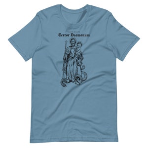 May include: A light blue t-shirt with a black and white illustration of Saint Joseph holding a baby. The text "Saint Joseph Terror Daemonum" is printed above the illustration.