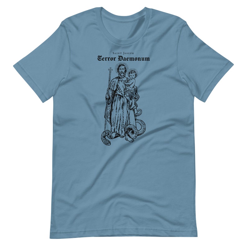 May include: A light blue t-shirt with a black and white illustration of Saint Joseph holding a baby. The text "Saint Joseph Terror Daemonum" is printed above the illustration.
