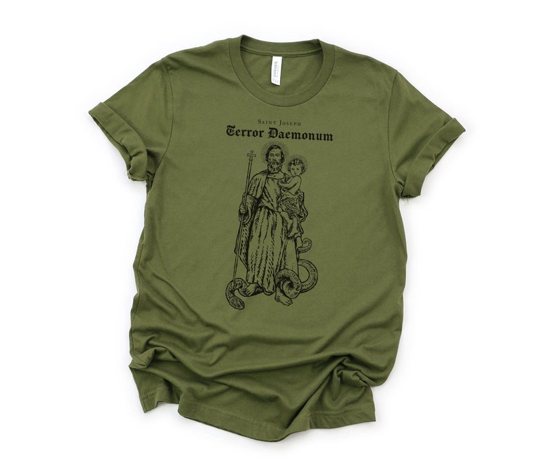 May include: A green t-shirt with a black and white illustration of Saint Joseph holding a baby. The text "Saint Joseph Terror Daemonum" is printed above the image.