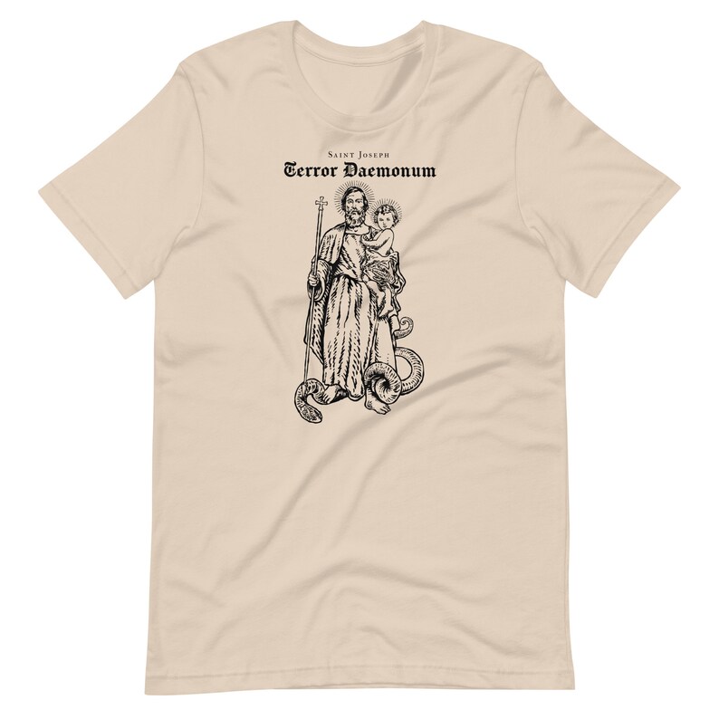 May include: A beige t-shirt with a black and white illustration of Saint Joseph holding a baby Jesus. The text "Saint Joseph Terror Daemonum" is printed above the illustration.