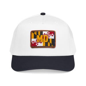 May include: A white baseball cap with a dark navy blue brim and a rectangular leather patch centered on the front. The patch features the Maryland state flag design with a distressed texture and the bold yellow letters MD printed in the center.