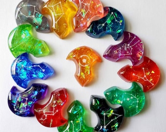 May include: A collection of colorful, resin-cast pendants in various shapes and colors, including green, blue, orange, and red. Each pendant features a constellation design with white lines and glitter accents. The pendants are arranged in a circular pattern.