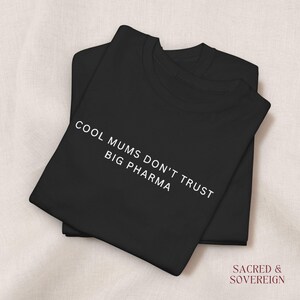 May include: A black short-sleeved t-shirt featuring the white text "COOL MUMS DON'T TRUST BIG PHARMA" printed on the front. The garment has a crew neckline and is folded neatly. The text "SACRED & SOVEREIGN" appears in the bottom right corner.