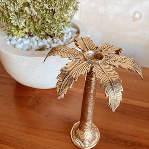 May include: A gold palm tree shaped decorative object with a textured surface. The palm tree is on a wooden surface.