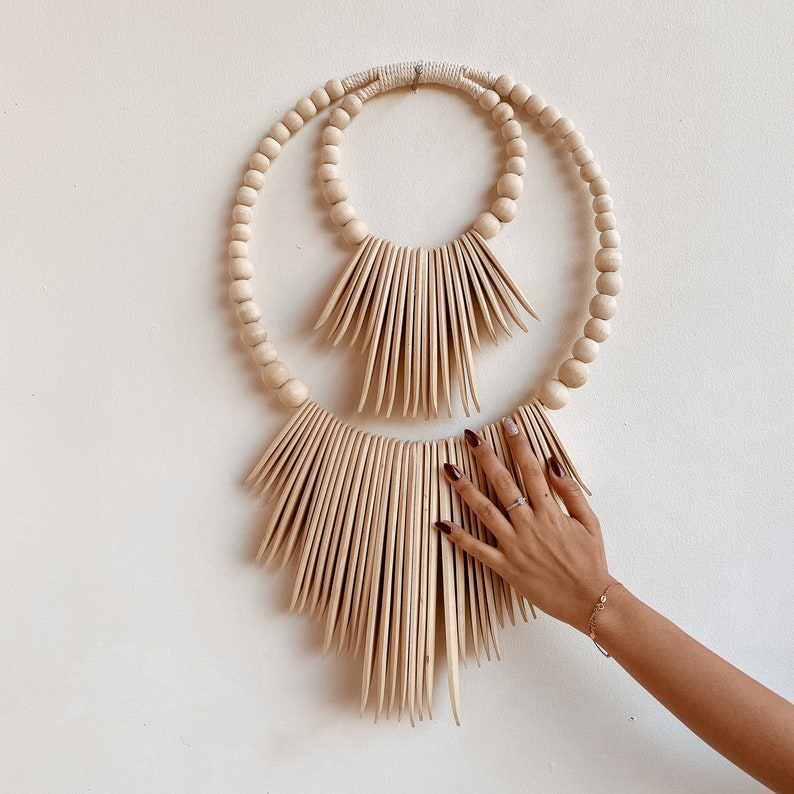 May include: A wooden wall hanging with two concentric circles of beads and a fan-shaped design of wooden slats.