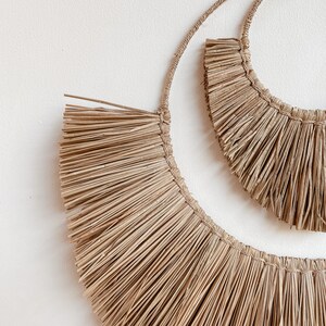 May include: Two natural woven straw wall hangings in the shape of half circles. The larger half circle is in front of the smaller half circle.