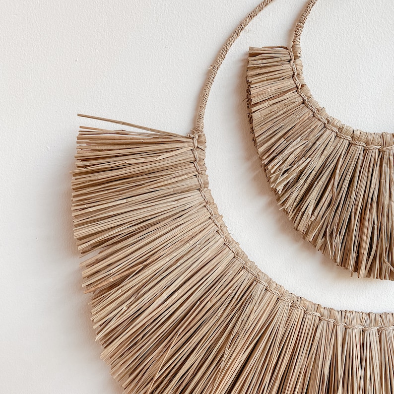 May include: Two natural woven straw wall hangings in the shape of half circles. The larger half circle is in front of the smaller half circle.