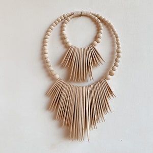 May include: A wooden wall hanging with two concentric circles of beads and a decorative fringe of wooden slats.