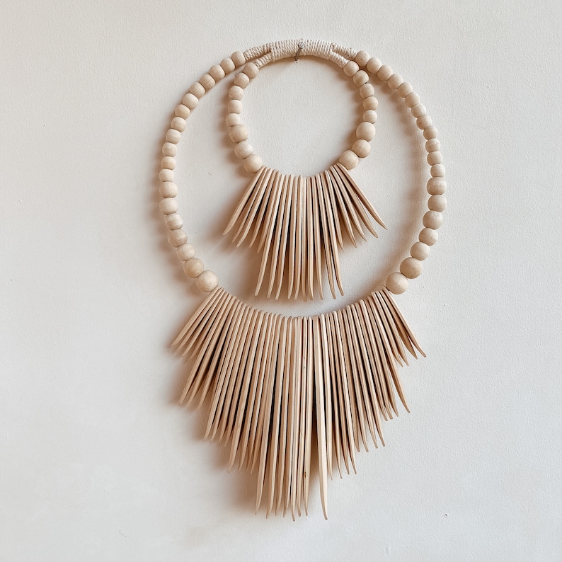 May include: A wooden wall hanging with two concentric circles of beads and a decorative fringe of wooden slats.