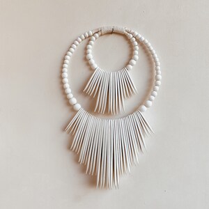 May include: White wooden bead wreath with two concentric circles and a fringe of white wooden slats.