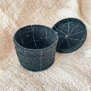May include: A black beaded round storage box with a lid. The box is made of small black beads woven together in a circular pattern.