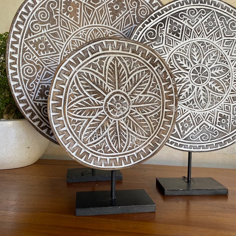 Puede incluir: Tres piezas redondas de decoraci&oacute;n de pared de madera con intrincados dise&ntilde;os tallados en blanco sobre un fondo marr&oacute;n. Cada pieza est&aacute; montada en un soporte negro.