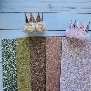 May include: Six strips of glitter fabric in various colors, including teal, gold, brown, rose gold, and pink. Two glitter crowns with white and pink flowers are on top of the fabric.