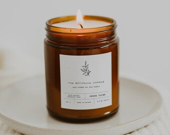 May include: A brown glass candle jar with a white label that reads "The Botanical Candle Co. Hand poured soy and coconut wax" and "Green Tea & Lime". The candle is lit and sitting on a white knitted blanket.