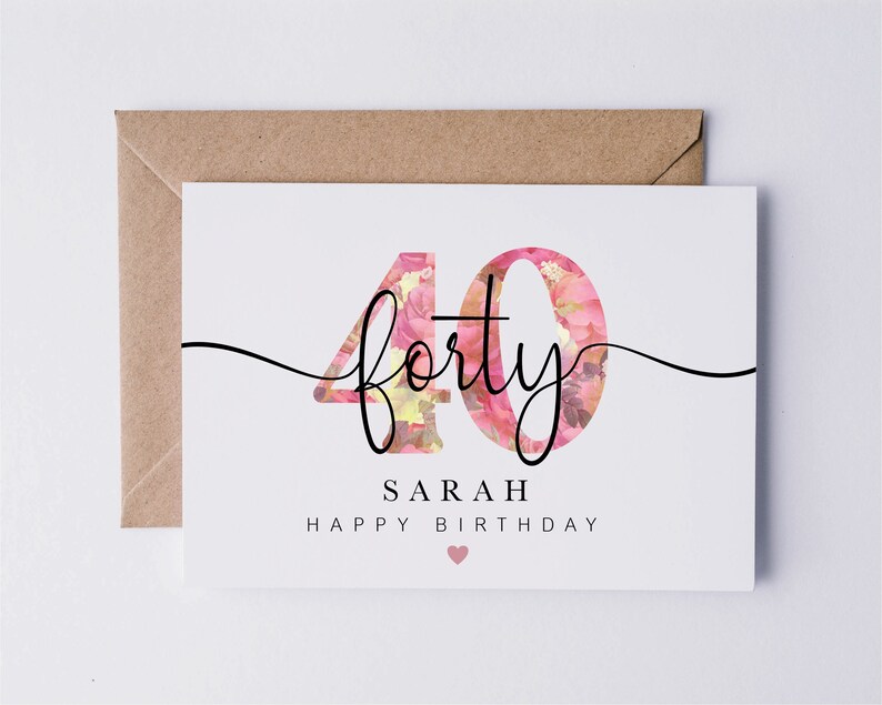 May include: A white card with a floral design in pink and yellow. The number 40 is written in black with the word "forty" written in cursive. The text "Sarah Happy Birthday" is written below the number. A small pink heart is at the bottom of the card.