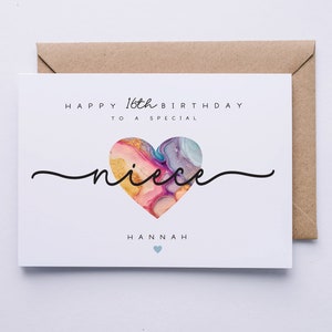 Puede incluir: Una tarjeta blanca con el texto "Happy 16th Birthday to a special niece Hannah" y un coraz&oacute;n colorido con detalles dorados.
