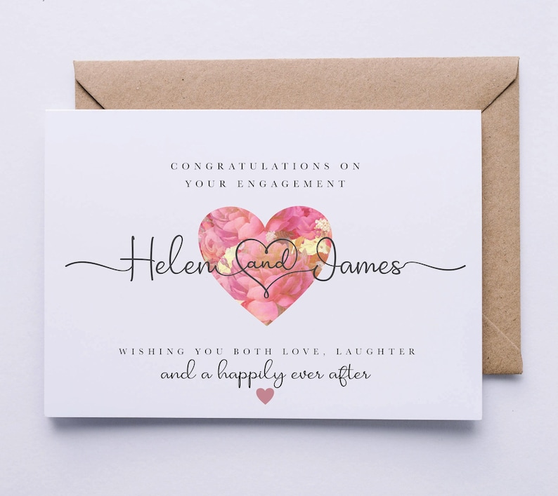 Puede incluir: Una tarjeta blanca con un coraz&oacute;n floral rosa y el texto "Felicidades por su compromiso Helen y James Les deseamos mucho amor, risas y un feliz para siempre".