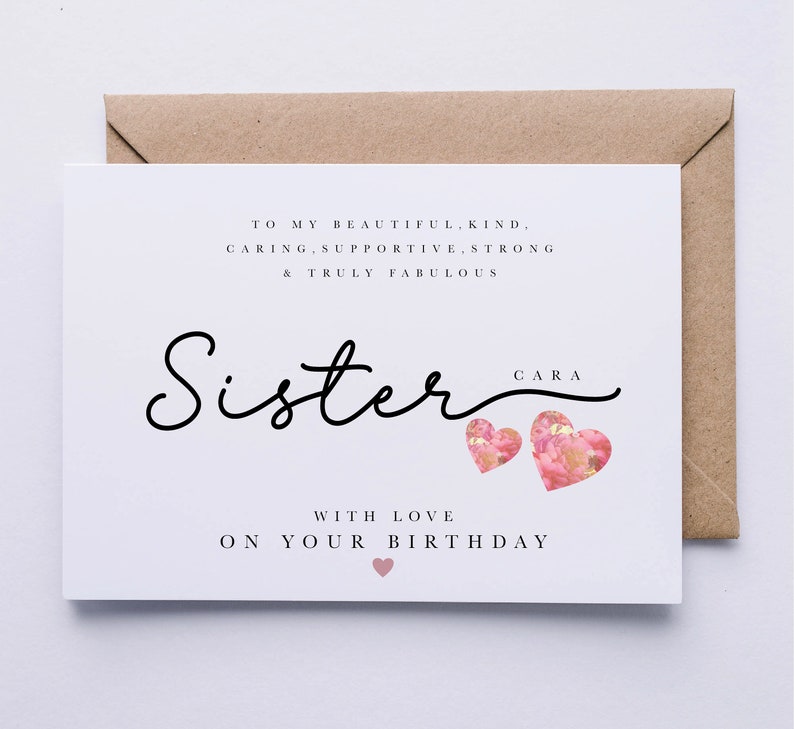Peut inclure: Une carte blanche avec du texte noir qui dit "To my beautiful, kind, caring, supportive, strong & truly fabulous Sister Cara with love on your birthday". La carte a deux c&oelig;urs roses avec des motifs floraux.