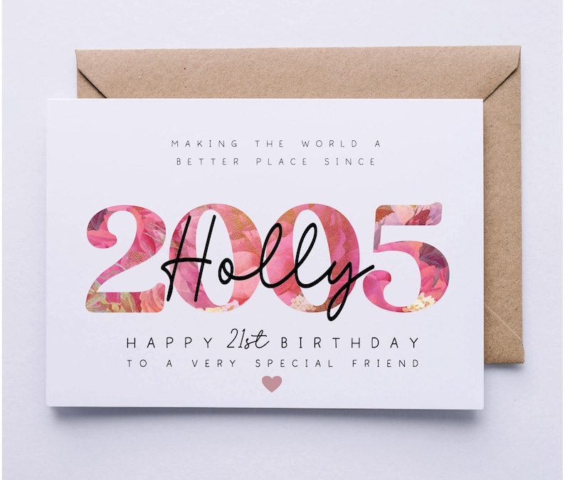 May include: A white birthday card with the name "Holly" in black script, set against a floral design within the numbers "2005". The card reads "Happy 21st Birthday" and is placed on a brown envelope.