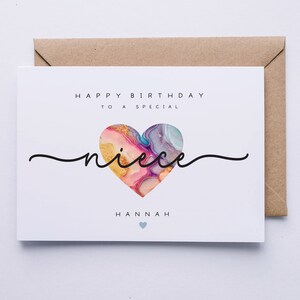 Puede incluir: Una tarjeta blanca con el texto "Feliz cumplea&ntilde;os a una sobrina especial Hannah" y un coraz&oacute;n colorido con detalles dorados.