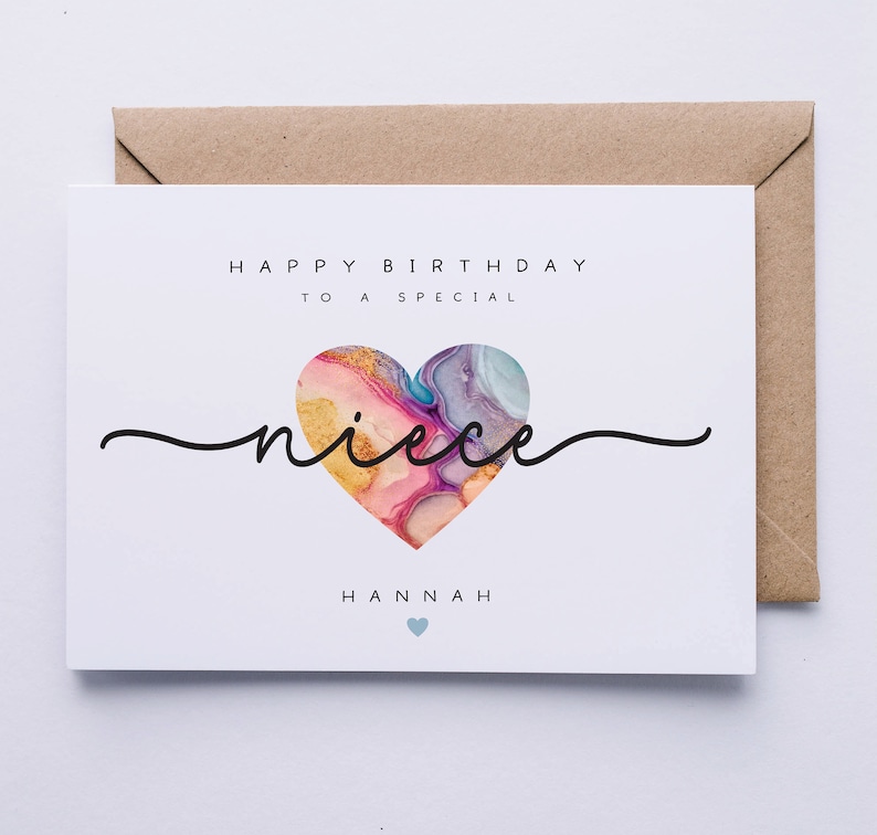 Puede incluir: Una tarjeta blanca con el texto "Feliz cumplea&ntilde;os a una sobrina especial Hannah" y un coraz&oacute;n colorido con detalles dorados.
