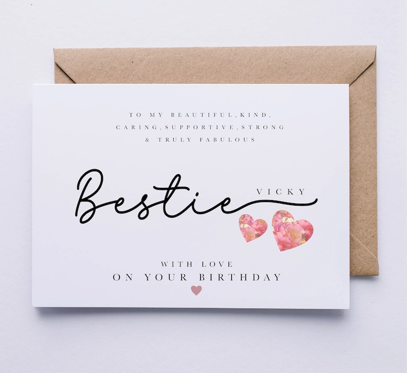 May include: A white greeting card with the word "Bestie" in cursive script, accompanied by two pink heart illustrations. The card includes text that reads "To my beautiful, kind, caring, supportive, strong & truly fabulous" and "With love on your birthday."