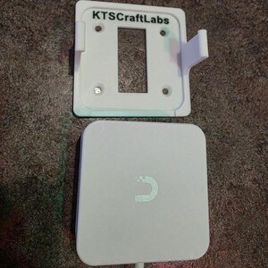 May include: A white wall mount with the text "KTSCraftLabs" above a rectangular aperture, and a white, square wireless charger with a curved design. A white cable extends from the charger.