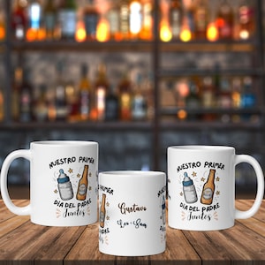 Puede incluir: Tres tazas de cerámica blanca con el texto "NUESTRO PRIMER DIA DEL PADRE JUNTOS" e ilustraciones de un biberón y una botella de cerveza. Una taza tiene los nombres "Gustavo Leo & Sam". Las tazas están sobre una superficie de madera.