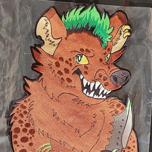 May include: Embroidered patch featuring a cartoon hyena with a menacing expression, holding a knife. The hyena has brown fur with dark spots, green eyes, and a green mohawk. The patch has a black border and is on a clear plastic sheet.