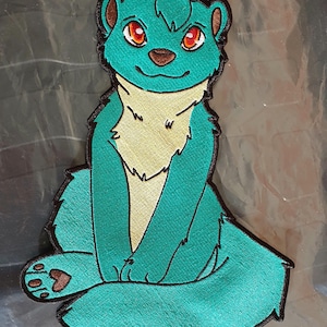 May include: Embroidered patch featuring a teal cartoon animal with red eyes, a tan chest, and brown accents. The patch is outlined in black and depicts the animal in a seated position, with its paws and tail visible.