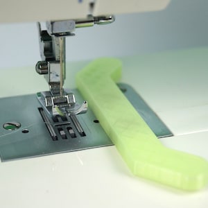 Peut inclure: Gros plan sur l'aiguille et le pied d'une machine à coudre avec un guide de couture en plastique vert placé à côté.