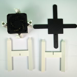 K&ouml;nnte beinhalten: Ein wei&szlig;er Plastik-Ventilatorst&auml;nder mit einem schwarzen Ventilator. Der St&auml;nder hat vier Beine und eine quadratische Basis. Der Ventilator hat einen schwarzen Grill und einen wei&szlig;en Rahmen.