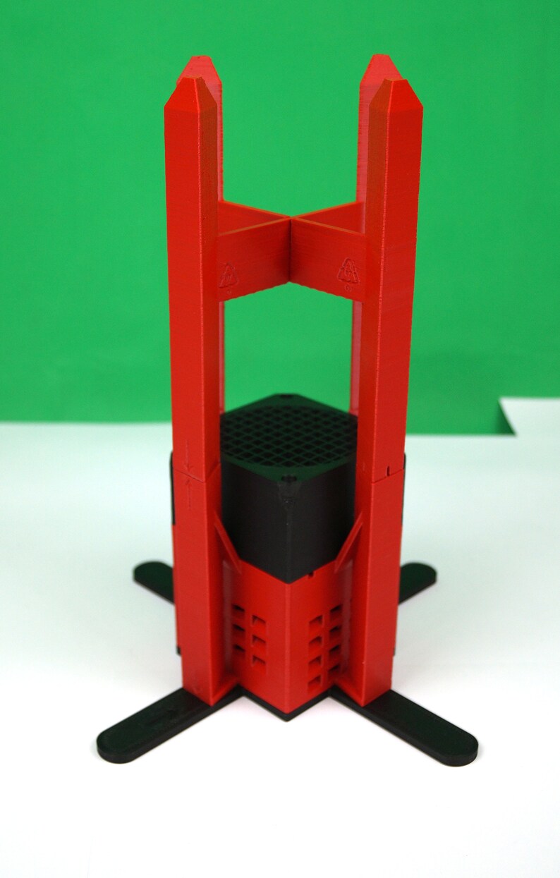 K&ouml;nnte beinhalten: Ein roter 3D-gedruckter St&auml;nder mit schwarzem Sockel und vier Beinen. Der St&auml;nder ist so konzipiert, dass er ein kleines Ger&auml;t oder Objekt h&auml;lt.