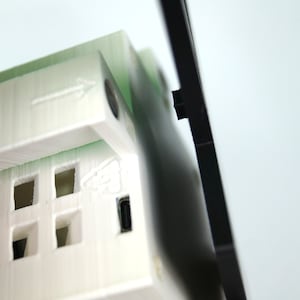 K&ouml;nnte beinhalten: Ein wei&szlig;es 3D-gedrucktes Modell eines Hauses mit einem schwarzen Rahmen. Das Haus hat an jeder Seite ein kleines Fenster und einen USB-Anschluss an der Unterseite.