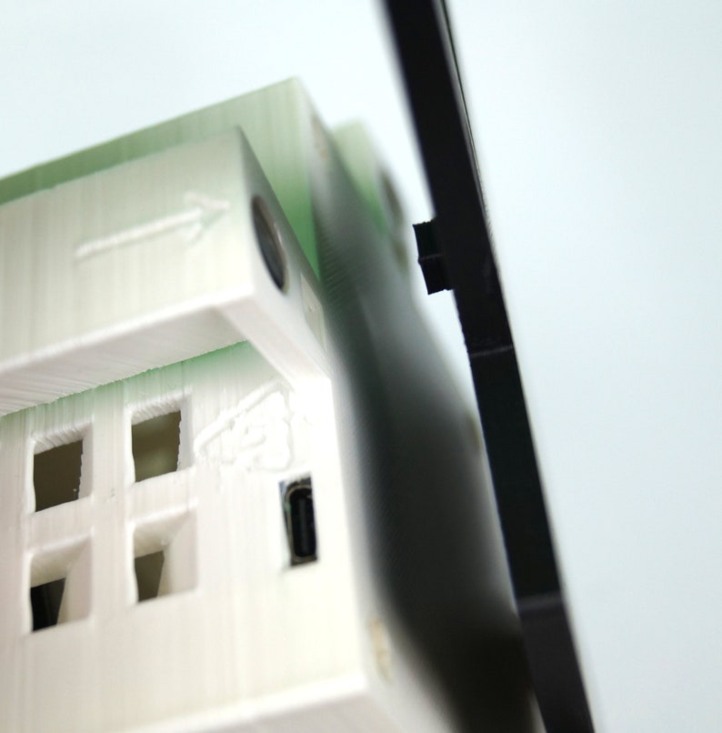 K&ouml;nnte beinhalten: Ein wei&szlig;es 3D-gedrucktes Modell eines Hauses mit einem schwarzen Rahmen. Das Haus hat an jeder Seite ein kleines Fenster und einen USB-Anschluss an der Unterseite.