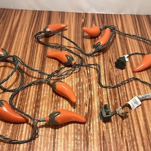 May include: A string of chili pepper shaped Christmas lights with a green wire and a plug. The lights are orange and green.