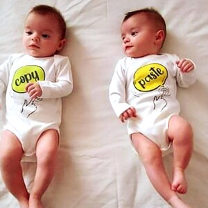 May include: Two babies wearing white long-sleeved onesies. One onesie has a yellow speech bubble with the word "copy" in green text. The other onesie has a yellow speech bubble with the word "paste" in green text.