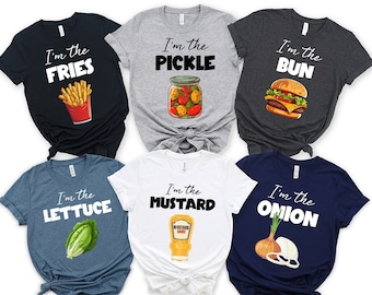 May include: Six t-shirts with different food-themed designs. Each shirt features a white graphic with black text that reads "I'm the" followed by the name of a food item. The shirts are in various colors, including navy blue, white, gray, and dark gray.