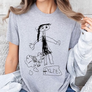 a woman sitting on a bed wearing a t - shirt with a drawing of a
