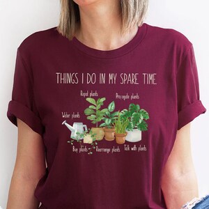 Peut inclure: Un t-shirt marron avec le texte "THINGS I DO IN MY SPARE TIME" et une liste d'activit&eacute;s li&eacute;es aux plantes, notamment "Repot plants", "Propagate plants", "Water plants", "Buy plants", "Rearrange plants", et "Talk with plants".