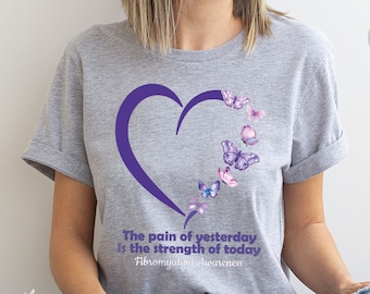 May include: Heather grey t-shirt with a purple heart and butterflies. The text on the shirt reads "The pain of yesterday is the strength of today Fibromyalgia Awareness".