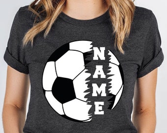 Può includere: Maglietta grigio scuro melange con un grafico di pallone da calcio bianco. La parola "NAME" è scritta verticalmente all'interno del pallone, con ogni lettera che appare in una sezione diversa del pallone.