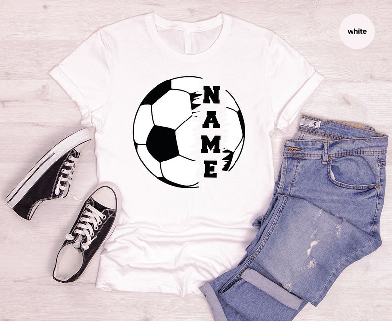 May include: White t-shirt with a black and white soccer ball graphic and the word "NAME" written vertically inside the ball.
