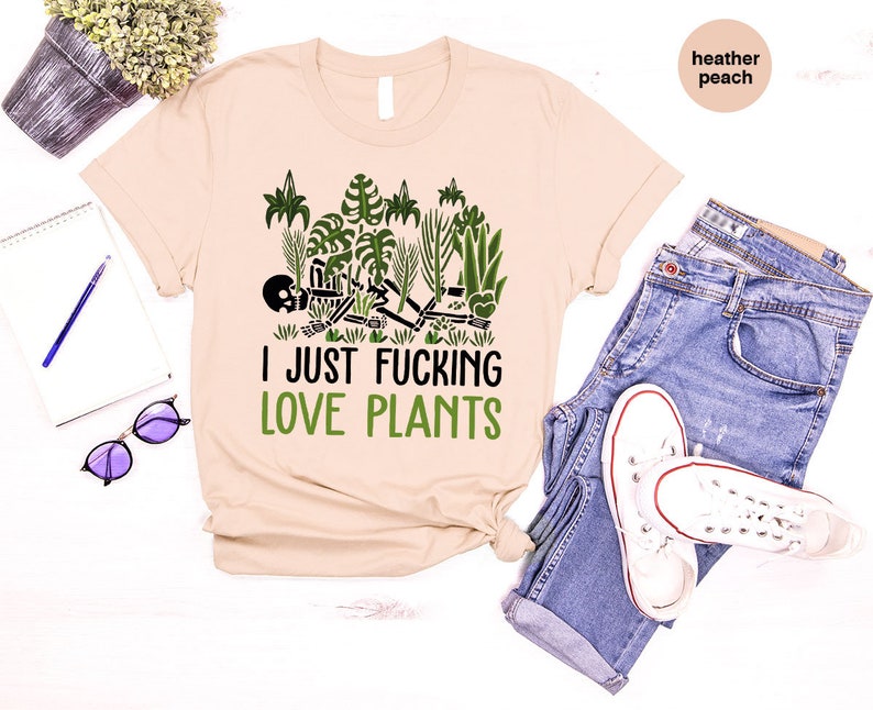 May include: A beige t-shirt with a green graphic of a skeleton surrounded by plants. The text "I JUST FUCKING LOVE PLANTS" is printed in green below the graphic.