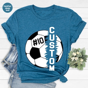May include: A heather deep teal t-shirt featuring a white football graphic with the word "CUSTOM" written vertically down the side of the ball. The football has a black number "10" on it.