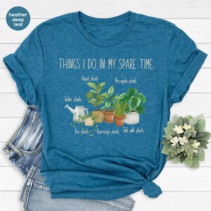 Peut inclure: Un t-shirt bleu sarcelle fonc&eacute; en coton m&eacute;lang&eacute; avec le texte "THINGS I DO IN MY SPARE TIME" et une liste d'activit&eacute;s li&eacute;es aux plantes, notamment "Arroser les plantes", "Rempotage des plantes", "Propager les plantes", "Acheter des plantes", "R&eacute;organiser les plantes" et "Parler aux plantes".