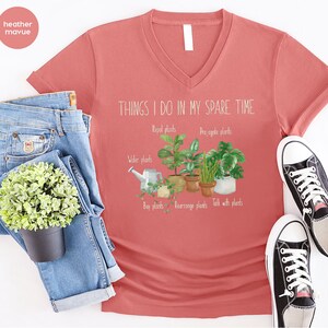 Peut inclure: Un t-shirt &agrave; col en V de couleur mauve heather avec le texte "THINGS I DO IN MY SPARE TIME" et un graphique de plantes en pot avec le texte "Repel plants", "Propagate plants", "Water plants", "Buy plants", "Rearrange plants", et "Talk with plants".