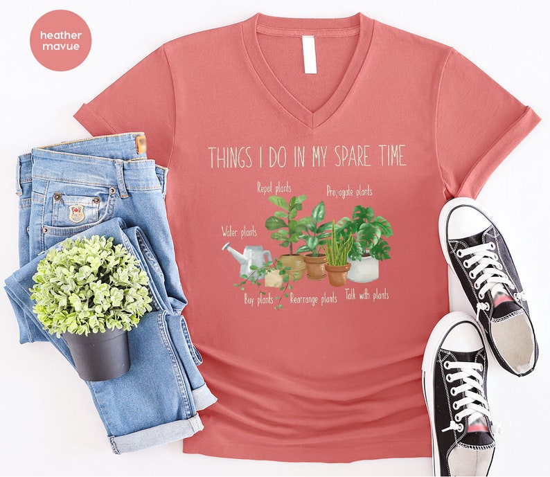 Peut inclure: Un t-shirt &agrave; col en V de couleur mauve heather avec le texte "THINGS I DO IN MY SPARE TIME" et un graphique de plantes en pot avec le texte "Repel plants", "Propagate plants", "Water plants", "Buy plants", "Rearrange plants", et "Talk with plants".