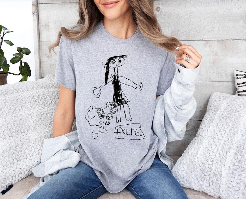 a woman sitting on a bed wearing a t - shirt with a drawing of a